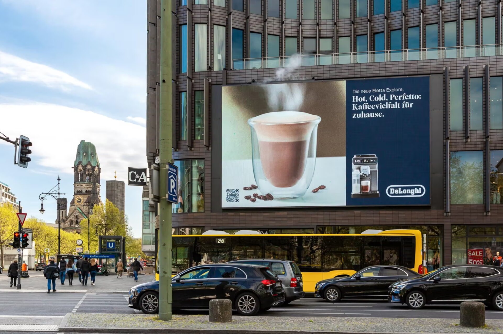 LED-Großformat am Berliner Ku'damm mit DeLonghi Periétto-Spot. Dampf steigt aus der Kaffeetasse auf der Leinwand auf — Kaiser-Wilhelm-Gedächtniskirche im Hintergrund.